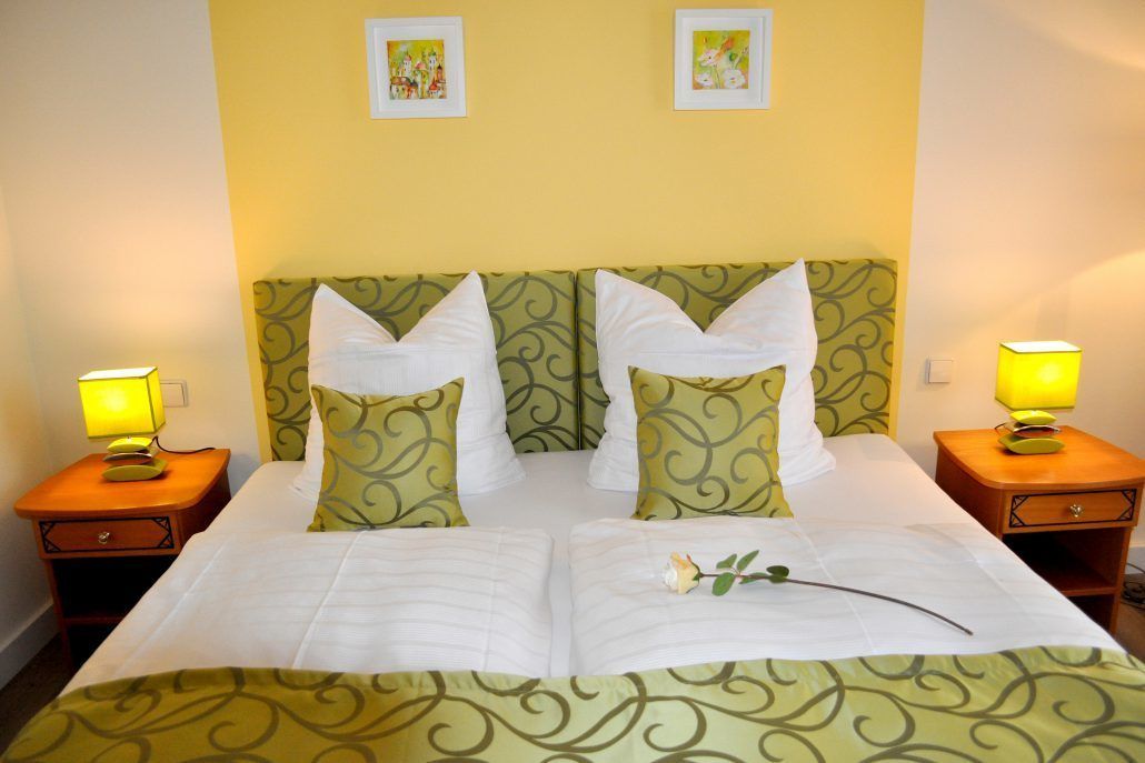 A double bed with a green patterned headboard, two bedside lamps, and a single white rose on the bed.