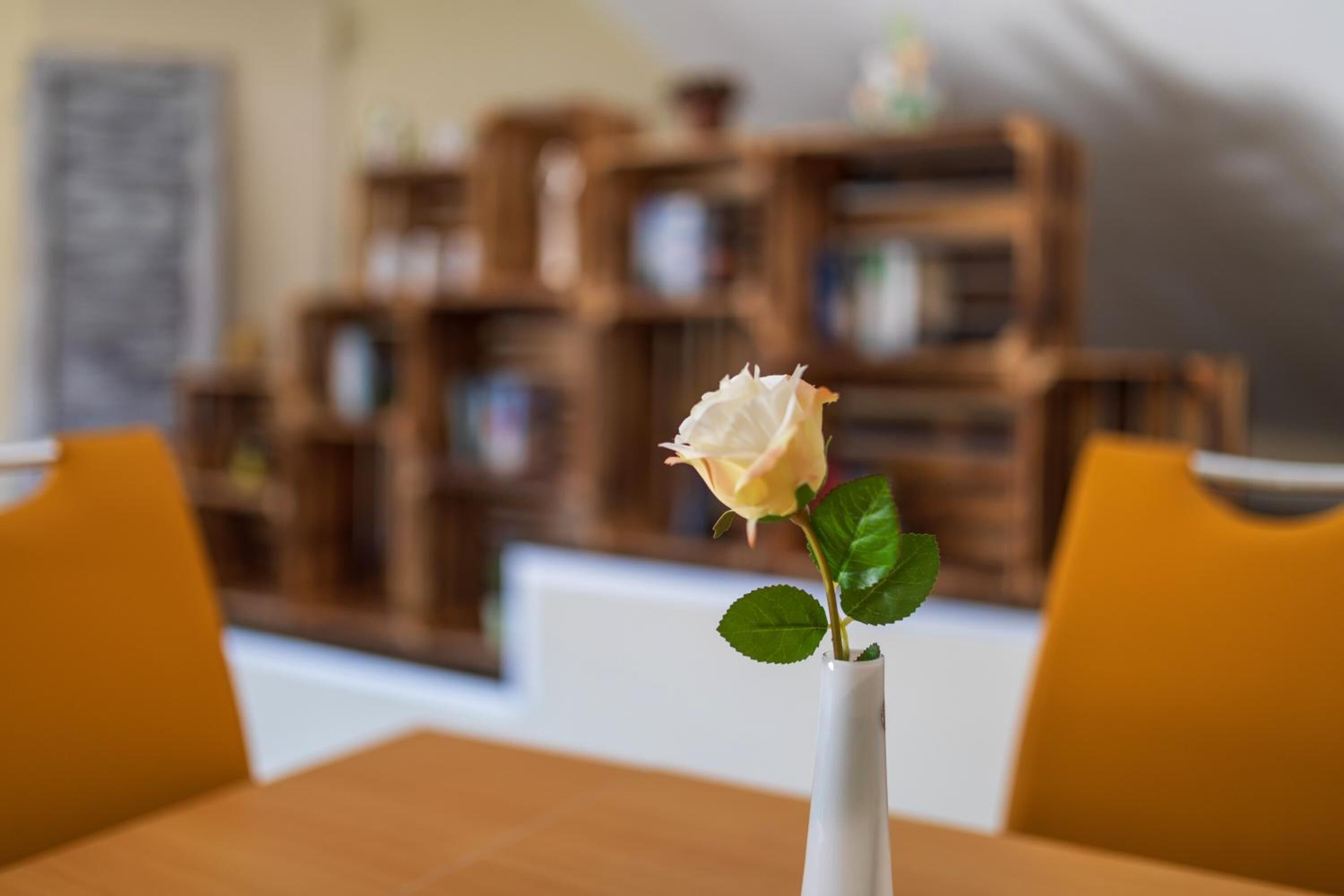 Eine weiße Vase mit einer weißen Rose auf einem Tisch.