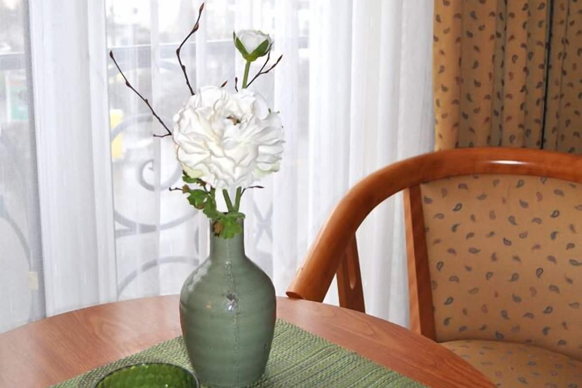 Una mesa de madera redonda con un jarrón verde que contiene flores blancas y un vaso de vidrio verde.