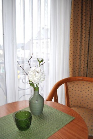 A round wooden table with a green vase containing white flowers and a green glass. - Landhotel Gillenfelder Hof (Gillenfeld)