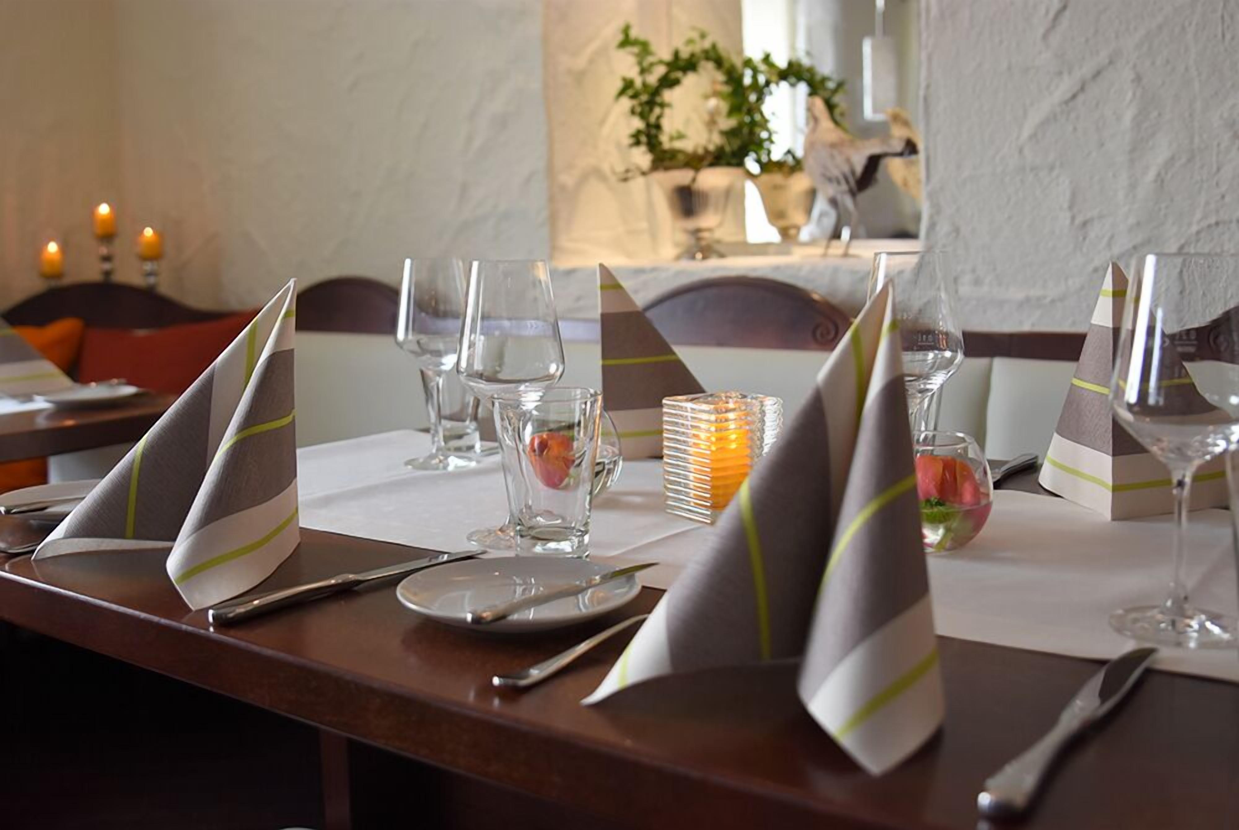 Una mesa de comedor lista con vajilla, cubiertos, copas y servilletas.