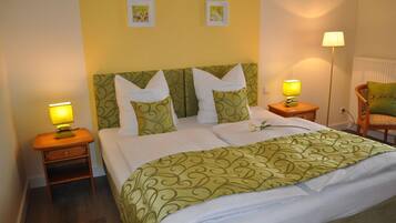 A neatly made bed with a green patterned bedspread, two white pillows, and a matching green headboard. There are two bedside lamps, one on each side of the bed.