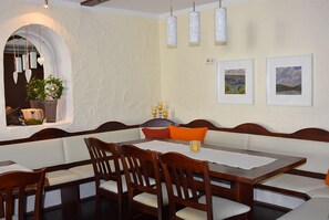 A dining area with a long wooden table, cushioned benches, and hanging pendant lights. - Landhotel Gillenfelder Hof (Gillenfeld)