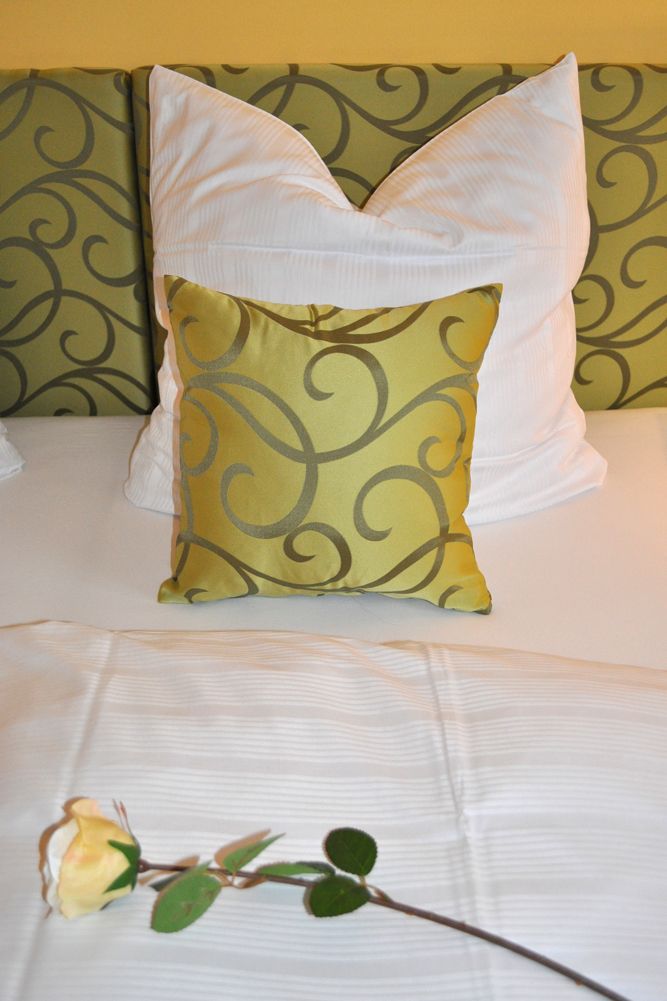A bed with a white pillow and a decorative pillow with a swirl pattern.