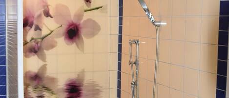 A shower with a floral design on the wall, a handheld showerhead, and a wall-mounted faucet.