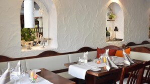 A restaurant with a rustic interior, featuring wooden tables and benches, white walls, and decorative elements like a bird sculpture and hanging plants. - Landhotel Gillenfelder Hof (Gillenfeld)