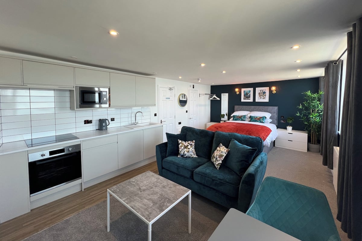 A compact living space with a kitchenette, a sofa, a bed, and a small table.