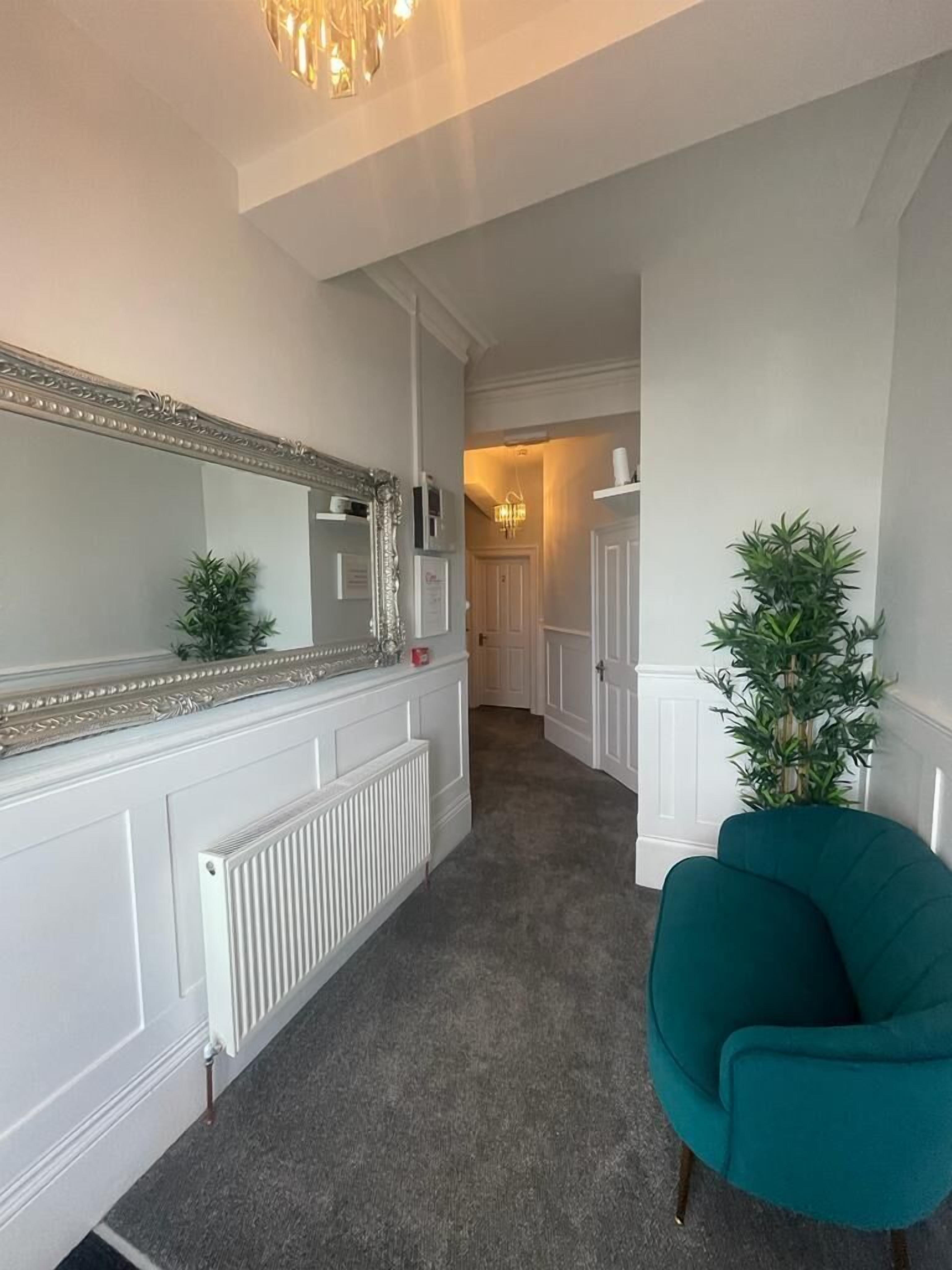 A hallway with a large mirror, a radiator, a teal chair, and a plant.