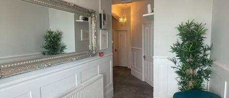 A hallway with a large mirror, a radiator, a teal chair, and a plant.