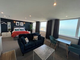 Habitación de hotel moderna con una cama grande, un sofá, un escritorio y vistas a la playa.