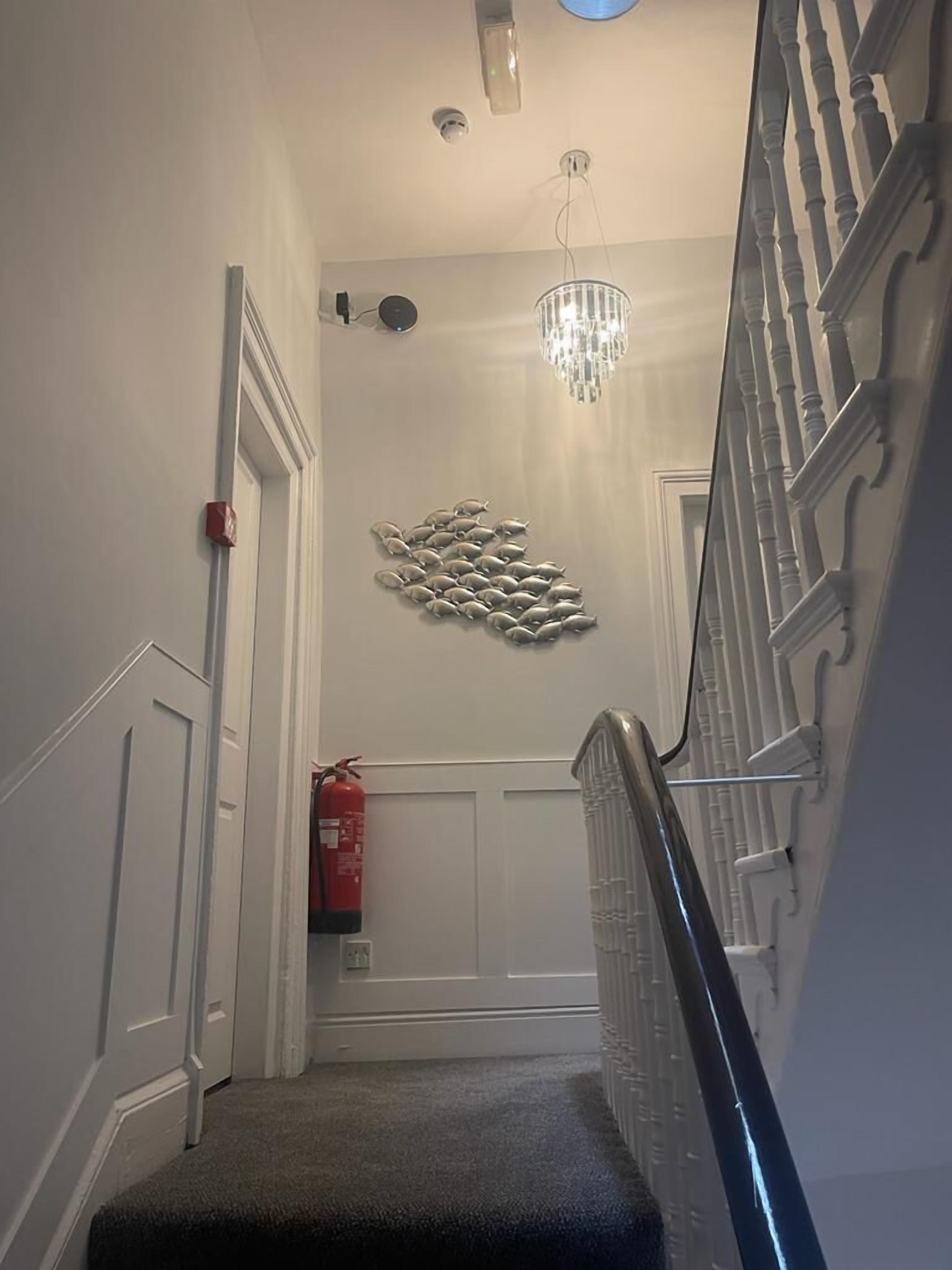 A hallway with a chandelier, a fire extinguisher, and a decorative wall piece.