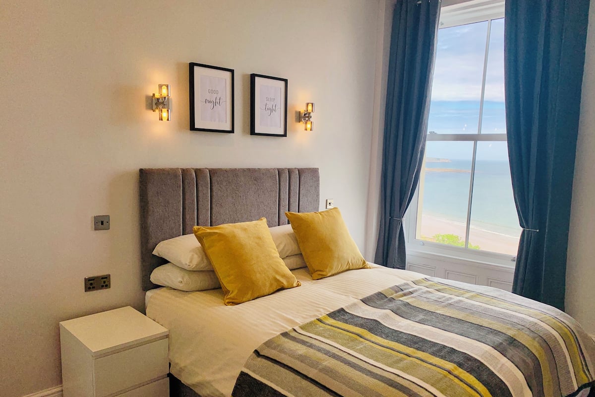 A bedroom with a bed, two wall-mounted lights, a nightstand, and a window with curtains.