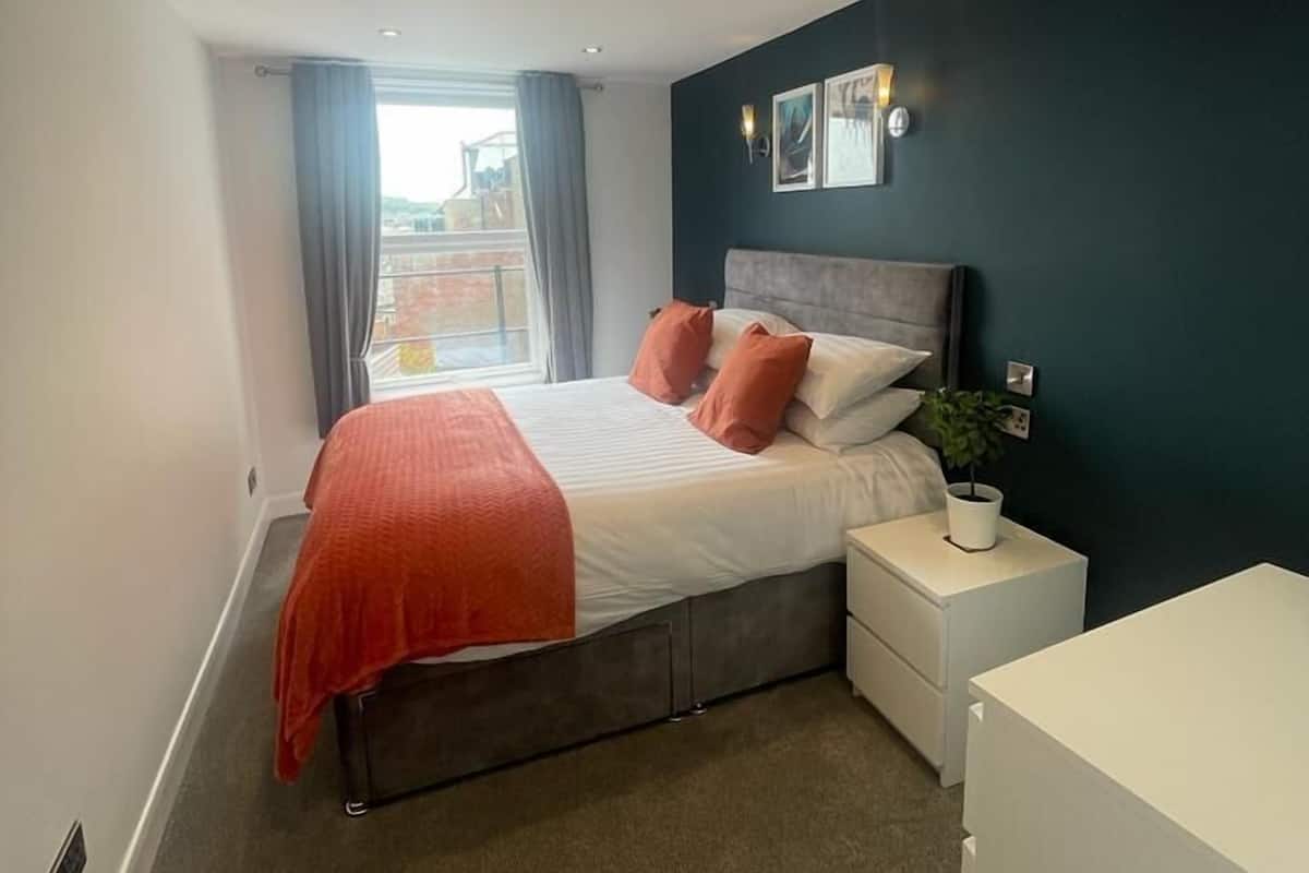 A modern bedroom with a bed, nightstands, a dresser, and a window with curtains.