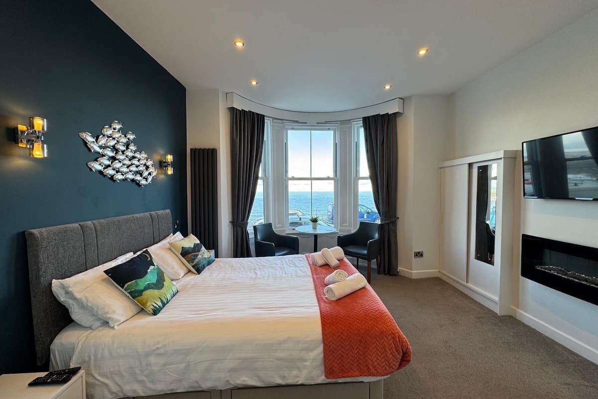 A modern hotel room with a large bed, a TV, a dining area with a view, and a balcony.