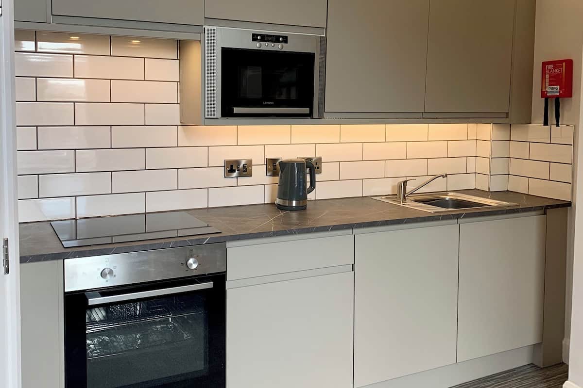 A modern kitchen with grey cabinets, a built-in oven, a microwave, and a kettle on the countertop.