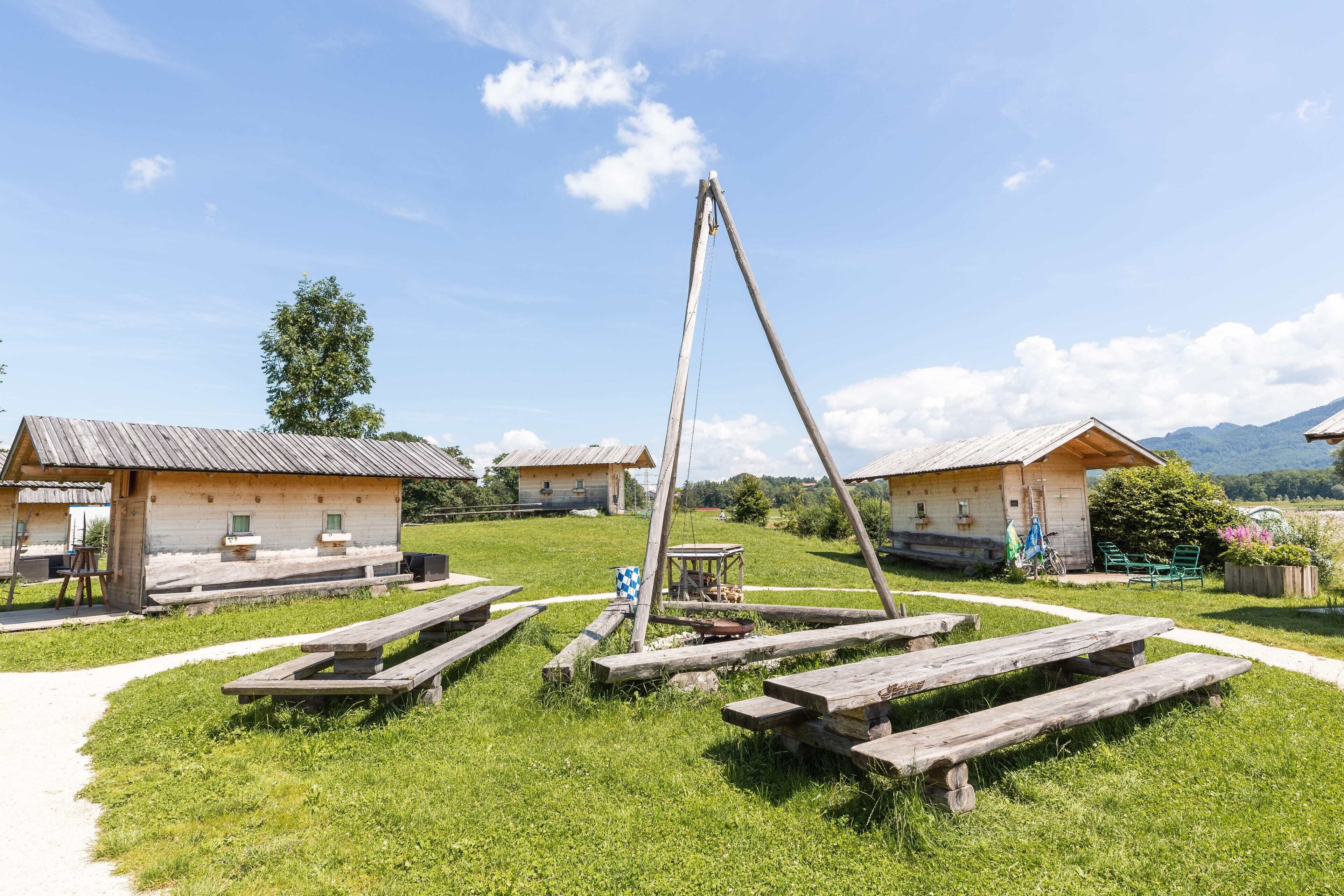 A rustic outdoor setting with wooden cabins, picnic tables, and a swing set.
