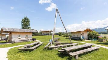 A rustic outdoor setting with wooden cabins, picnic tables, and a swing set.