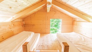 Una cabaña de madera con dos camas, techo inclinado y ventana con vista a la vegetación.