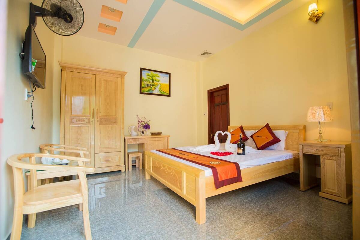 A hotel room with a bed, desk, chair, wardrobe, and a painting on the wall.