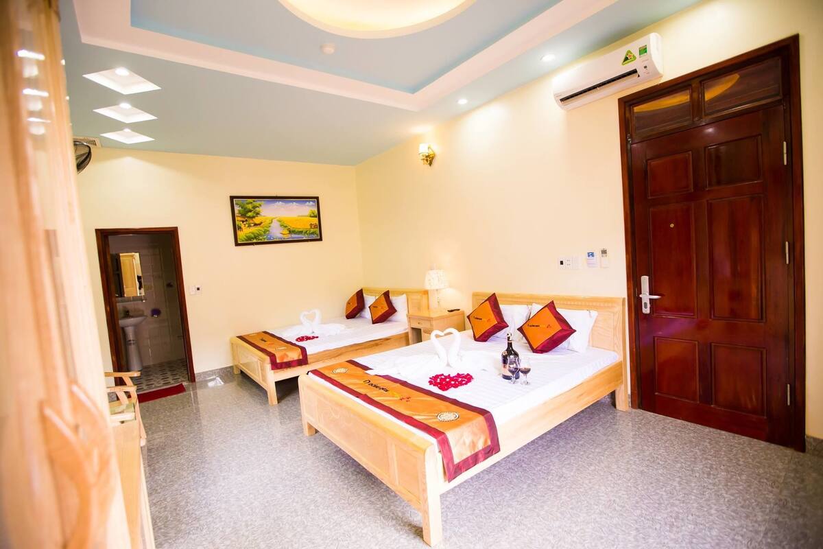 A hotel room with two beds, a wooden door, a painting on the wall, and an air conditioning unit.