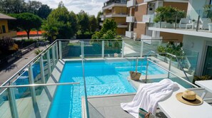 A rooftop swimming pool with glass railings, a white towel, and a straw hat on a table.