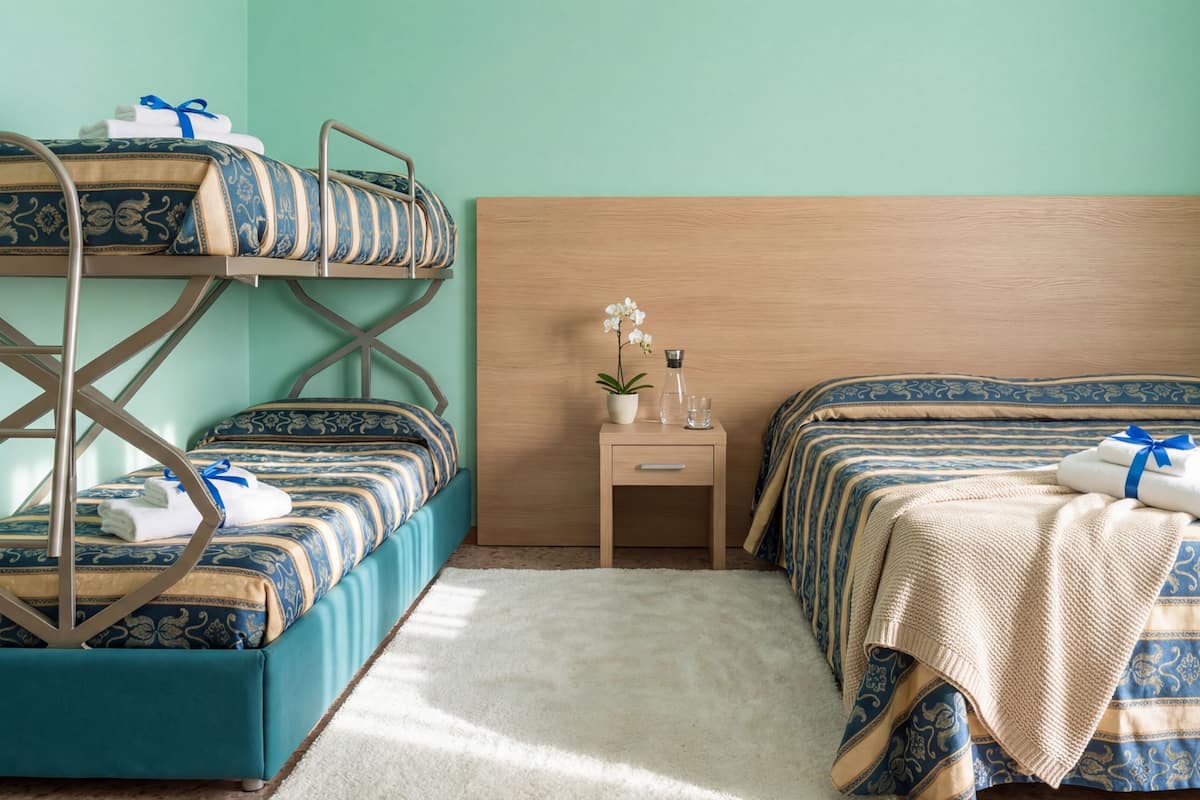 A room with bunk beds, a bedside table with a plant, and a nightstand with a glass.