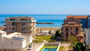 A coastal residential area with a view of the sea, a swimming pool, and a rocky breakwater.