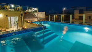 A rooftop swimming pool with a glass balustrade, steps leading into the water, and a view of the cityscape at night.