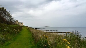 Ein Küstenpfad, der zu einem Haus mit Meerblick und einer entfernten Insel führt.