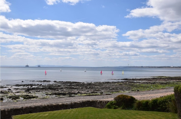 A coastal landscape with a grassy foreground, rocky shore, and a calm sea.