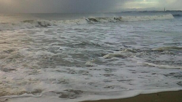 Ein Strand mit Wellen und bewölktem Himmel.