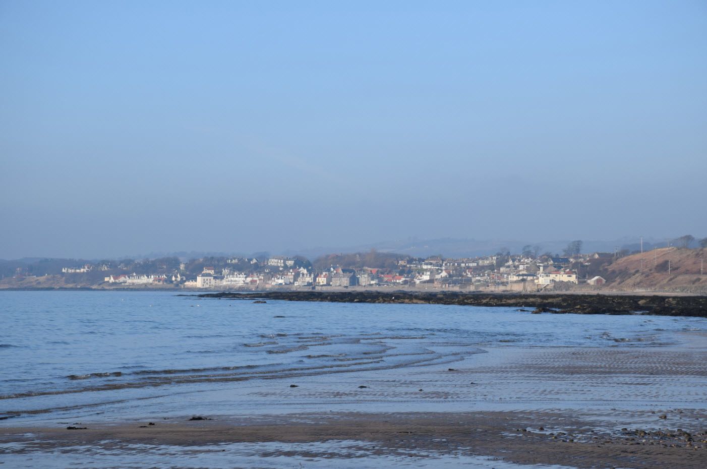 A coastal town with buildings along the shore, a sandy beach, and calm water.