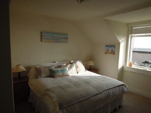 A bedroom with a bed, two bedside tables, a window, and a painting on the wall.