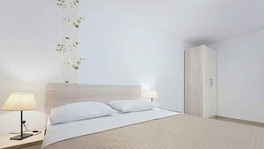 Un lit bien fait, avec du linge de lit blanc, une table de chevet avec une lampe et une armoire.