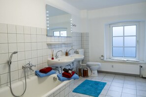 Ein modernes Badezimmer mit einer Badewanne, zwei Waschbecken, einer Toilette und einem Fenster.