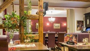 A restaurant interior with wooden beams, red walls, and a chandelier. Tables are set with menus and a 'Merry Christmas' sign.