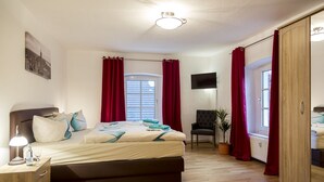 A bedroom with a bed, bedside table, lamp, TV, chair, potted plant, and a wardrobe.