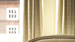 A beige sofa with a patterned cushion, positioned in front of a window with patterned curtains. - The Northgate (Bury St Edmunds)