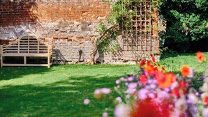 A wooden bench, a brick wall, and a garden with flowers. - The Northgate (Bury St Edmunds)