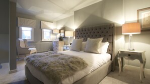 A bedroom with a large bed, a chair, a dresser, and a nightstand with a lamp. - The Northgate (Bury St Edmunds)