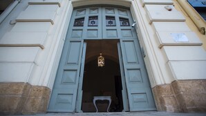 A building entrance with a large arched doorway, a hanging light fixture, and a small table with a vase.