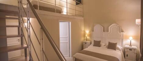 A bedroom with a double bed, a nightstand, a bedside lamp, a staircase, and a door leading to another room.