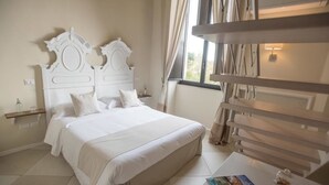 A neatly arranged bedroom with a large bed, a bedside table with a book and a glass, and a window with curtains.