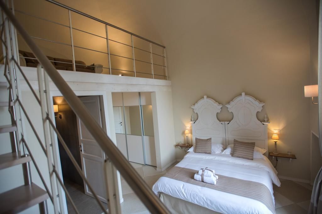 A bedroom with a large bed, a headboard with decorative elements, bedside lamps, and a view of a staircase leading to a loft area.