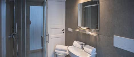 Un baño moderno con cabina de ducha de vidrio, un lavabo blanco y un espejo grande.