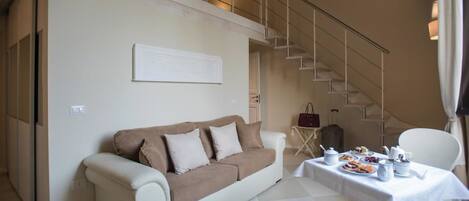 A modern living room with a sofa, a dining table set with dishes, and a staircase.