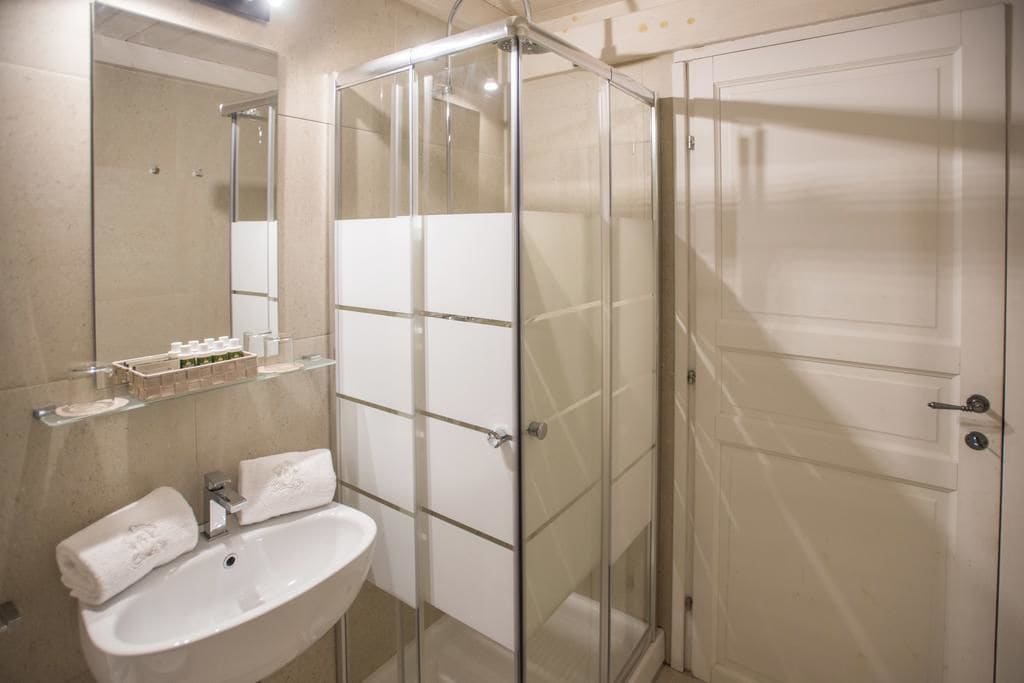 A bathroom with a glass shower enclosure, a white sink, and a mirror.