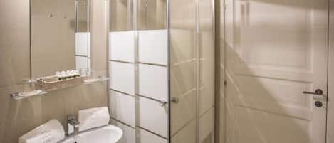 A bathroom with a glass shower enclosure, a white sink, and a mirror.
