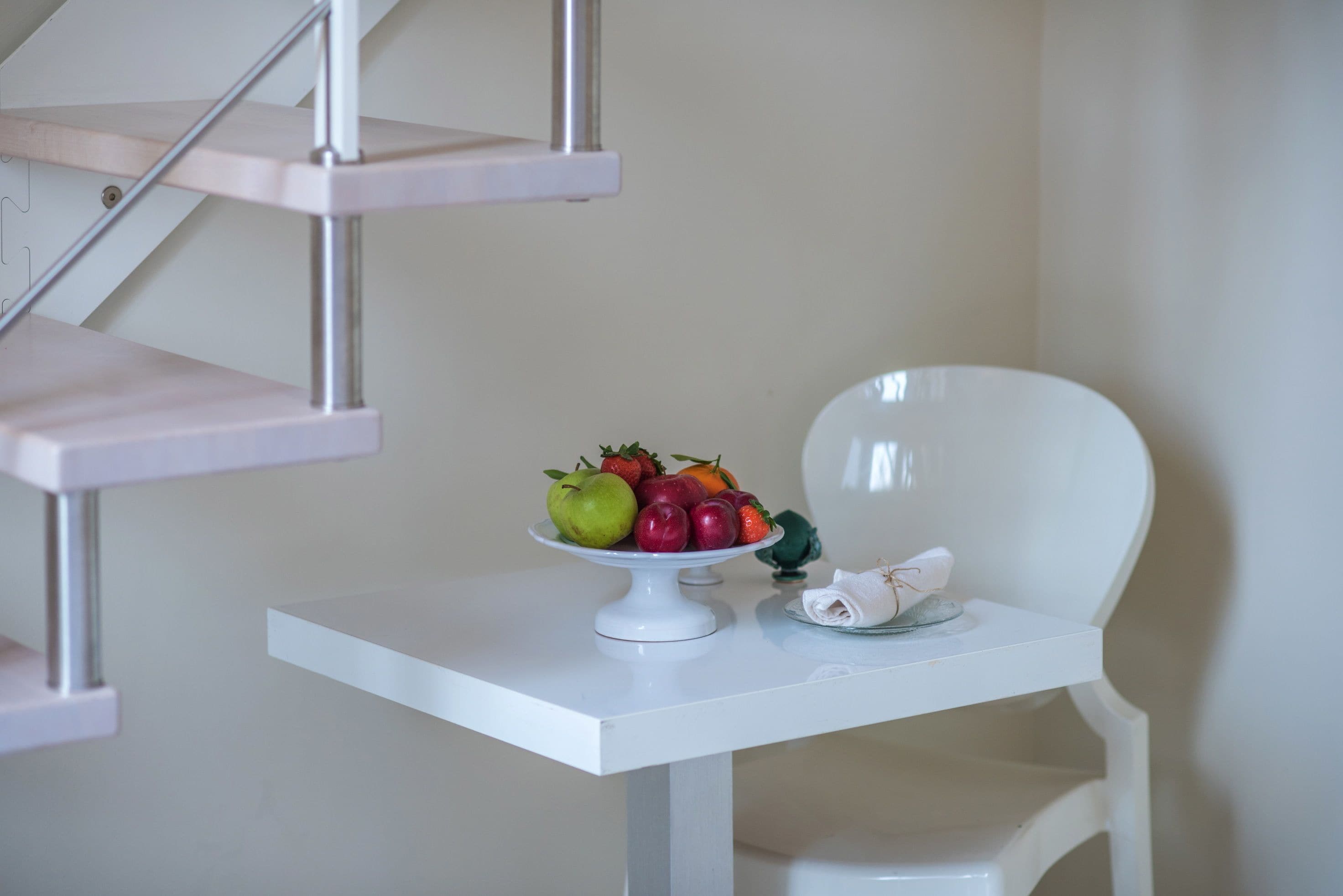 Una mesa blanca con un frutero y un paño doblado.