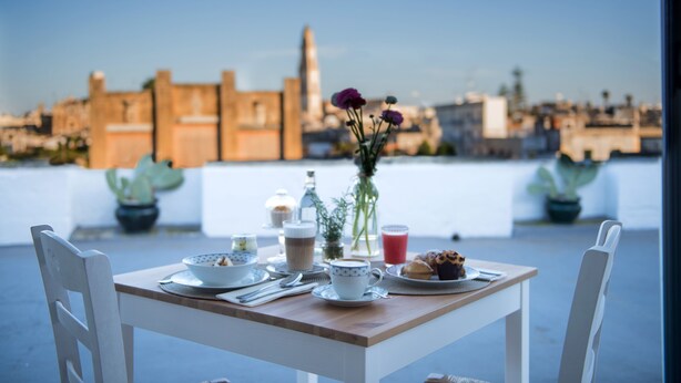 A table set with breakfast items, a vase with flowers, and a city view in the background.